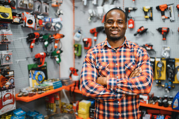 Confident smiling salesman on foreground in power tools store. Guy is ready to help clients on...