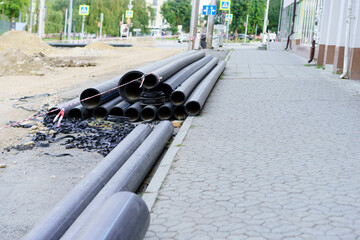 Construction activities on city street with stacked pipes and unfinished pavement during daytime