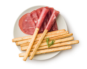 Slices of smoked bresaola and grissini sticks isolated on white background.