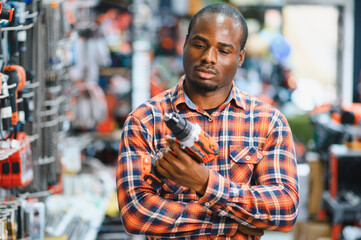 Obraz premium African americam man buying modern electric drill while standing in tool. Hardware construction site objects concept