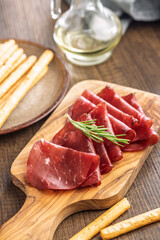 Slices of smoked bresaola on cutting board on wooden table.