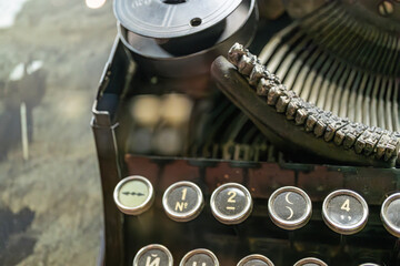 Antique metal typewriter with English lettering, in focus against a blurred background with natural light QWERTY layout, signs of age and wear, good condition for its age