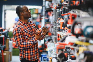 African americam man buying modern electric drill while standing in tool. Hardware construction...