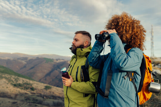 Hikers exploring mountain peaks, woman using binoculars, man holding reusable water bottle