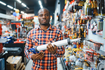 African american male customer in a modern hardware store chooses a silicone gun