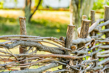 Ancient Central European village setting with a rustic twig and branch fence, aged and textured, in shades of brown, knotted and interwoven Softly blurred lush green background suggests trees or fol