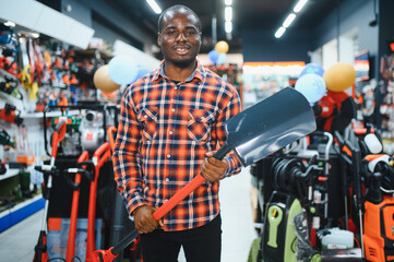 African American male customer in a garden tools store chooses a new shovel for earthworks
