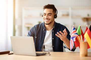 Positive arab guy tutor having online class with student, using laptop and headset at home....