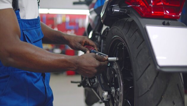 Skilled Hands at Work: Mechanic in Blue Overalls Meticulously Services a Motorcycle's Rear Wheel