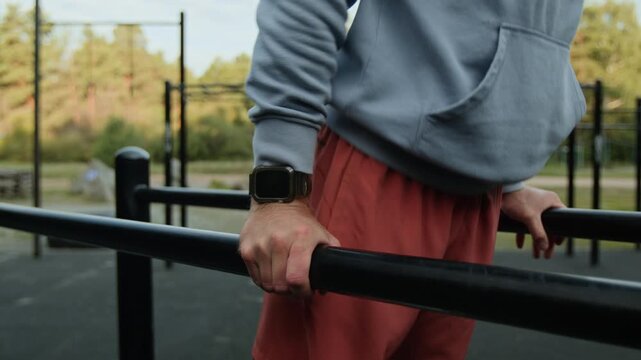 Close-up shot of unrecognizable man, wearing sportswear and smartwatch, doing dips on parallel bars in outdoor gym