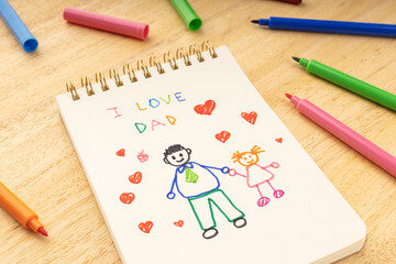Fathers day concept. Notebook with drawing of a father with a girl and marker pens on a wooden table