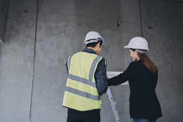 Construction manager and engineer dressed in orange work vests and hard helmets explore...