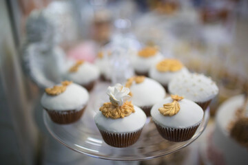 Cupcakes decorated with white fondant and golden floral accents, displayed elegantly on a glass tray. Perfect for a wedding or luxury party.