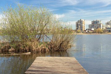 A small wooden pier on the bank of a river with residential buildings along the bank