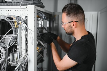 A technician works with server equipment in a data center. A man commutes wires in a server room