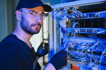 Young man is working with internet equipment and wires in server room
