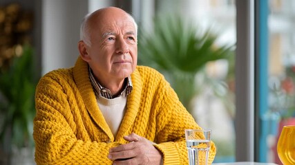 Man is waiting patiently in a bright room, lost in thought. Soft natural light fills the space, creating a calm atmosphere. Concept of elder care, wellness, mental health