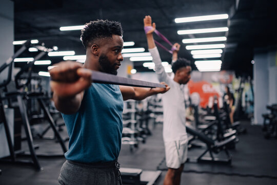 Determined black men performing resistance band exercises in gym