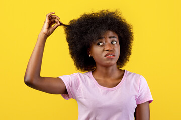 Upset african american lady touching and showing her curly hair on yellow background, studio shot....