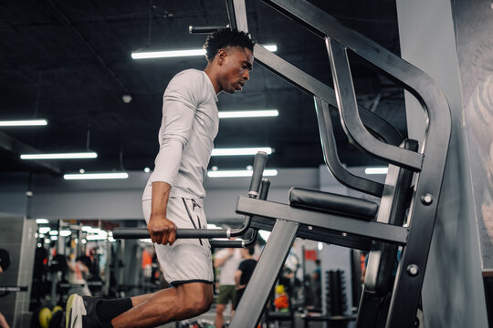 Determined male athlete performing dips on parallel bars in modern gym