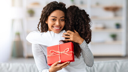 Curly black girl making birthday surprise for her excited mom, home interior, copy space. Happy...