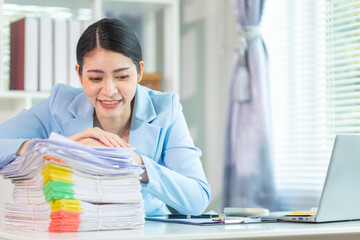 businesswoman is searching through documents to review large number of investment documents stacked...