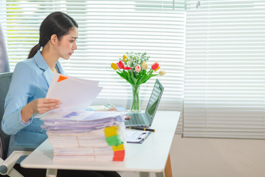 Businesswoman stressed searching for documents to check accounts and analyze business plan from a large number of documents on her desk. Businesswoman stressed over a large number of documents