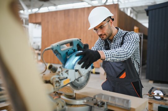 Professional carpenter using sawing machine for cutting wooden board at sawmill