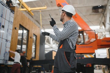 A worker controls the process of loading a modular house onto a truck. Transportation and delivery...