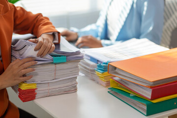 businesswoman and her secretary are helping search for documents examine large number investment documents piled on desk. businesswoman is having trouble finding large number documents piled on desk.