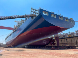 Large container ship in dry dock with stern, hull, and propeller visible during maintenance. © Maritime Art Blog
