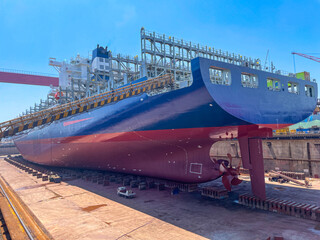 Large container ship in dry dock with stern, hull, and propeller visible during maintenance.