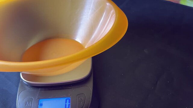 Weighing of pasta to be made in broth. Raw pasta is poured into an orange container placed on a black digital kitchen scale, black background