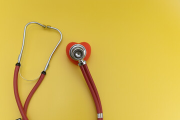 red stethoscope with red heart on yellow background, cardiologist's instruments