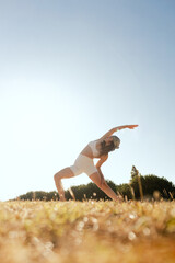 Young woman in sportswear stretching body on fitness mat at public park, doing yoga. Healthy...