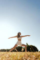 Young woman in sportswear stretching body on fitness mat at public park, doing yoga. Healthy...