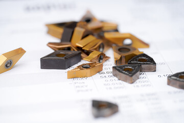 Collection of metal cutting inserts on technical specifications paper in a workshop