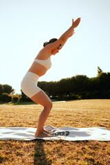Young woman in sportswear stretching body on fitness mat at public park, doing yoga. Healthy...