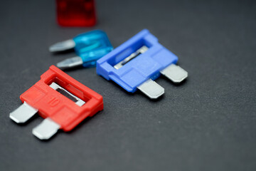 Colorful electrical fuses arranged on a dark surface, showcasing various sizes and designs for...