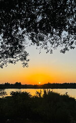 Obraz premium A picturesque natural phenomenon where the setting sun creates a vibrant sky, whose colours reflect on the calm, mirror-like surface of the water, often enhanced by silhouetted trees on the horizon.