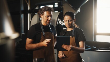 Man gesturing with one hand while standing beside woman reviewing tablet screen. Discussing coffee...