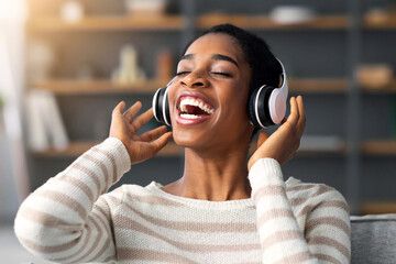 Favorite Playlist. Excited Happy Black Lady Enjoying Listening Music In Wireless Headphones While Relaxing On Couch In Cozy Living Room, Portrait Of Cheerful African American Woman In Headset