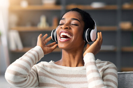 Favorite Playlist. Excited Happy Black Lady Enjoying Listening Music In Wireless Headphones While Relaxing On Couch In Cozy Living Room, Portrait Of Cheerful African American Woman In Headset - Powered by Adobe