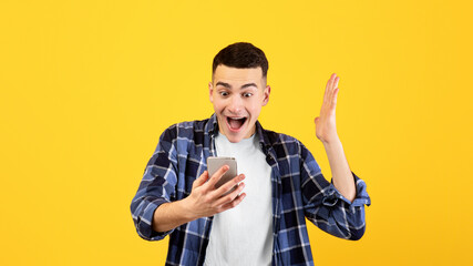 Excited millennial guy in casual outfit looking at smartphone, happy over his win or success on...