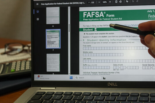 A person pointing at the FAFSA Form (Free Application for Federal Student Aid) with a stylus pen at a desk. College preparation, economy, and education design element. Editorial Use Only.