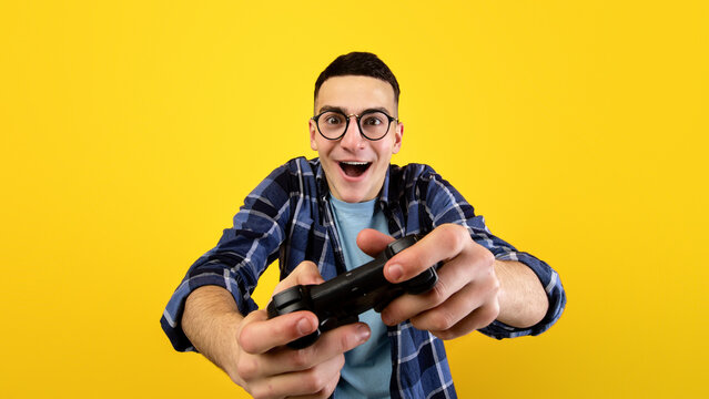 Happy Caucasian guy with joystick playing video game on orange studio background. Young computer gamer with controller enjoying online gaming competition. Stay home hobbies and pastimes