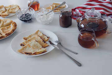 Traditional crepes with jam, sour cream and tea served on white table. Top view, cozy homemade...