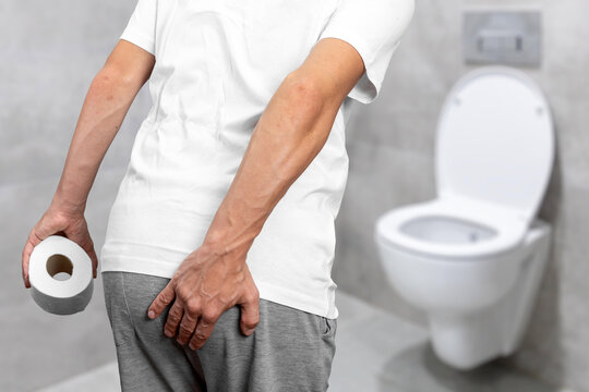 Man suffering from hemorrhoids or rectal pain holding his backside in bathroom, concept of digestive health issues, constipation, anal itching, prostate problems, and urinary tract infection symptoms.