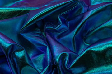 Close-up of iridescent metallic fabric with shimmering folds in blue, green and violet tones,...
