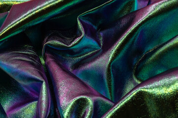 Shimmering iridescent fabric with folds in green, purple and blue tones, reflecting light with...